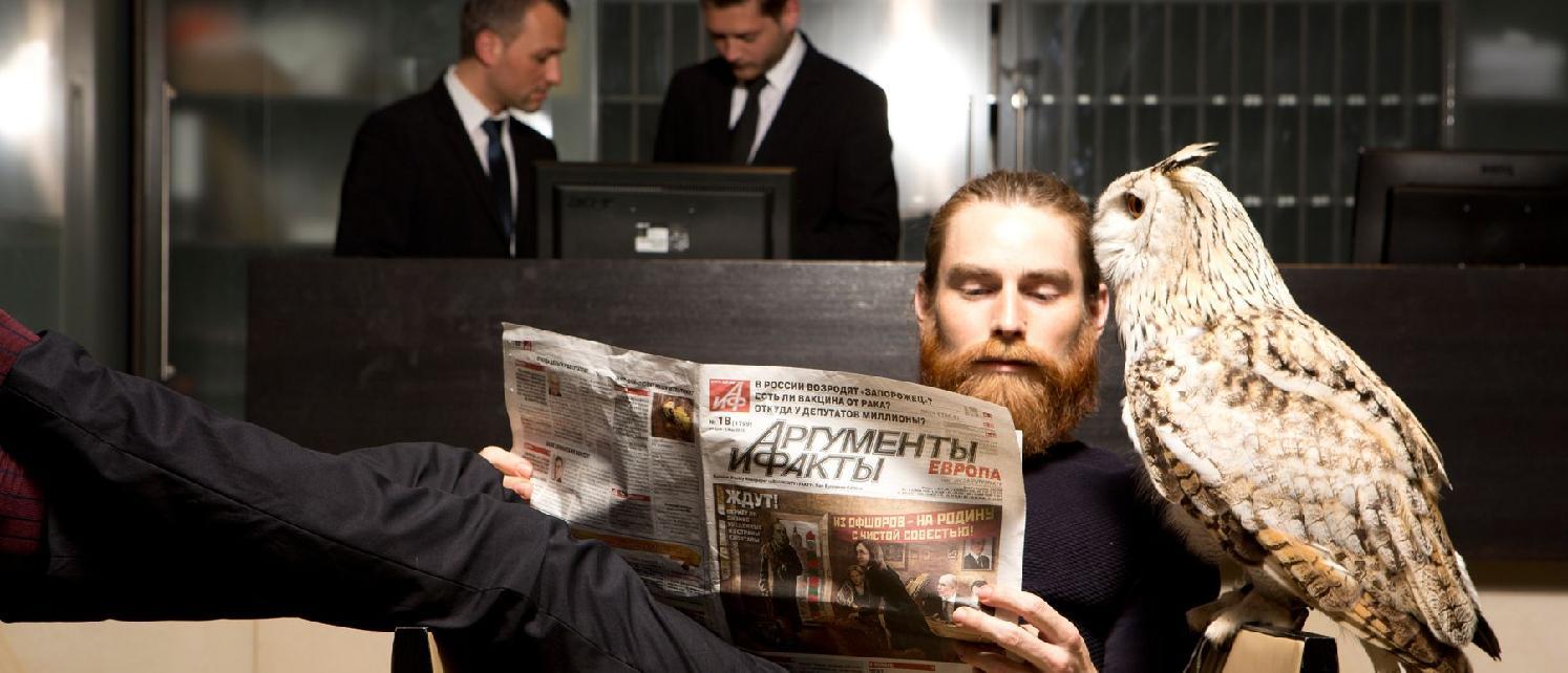 Townhouse Dresden Hotel Exterior photo The photo depicts a man with a long beard reading a newspaper while sitting comfortably. He has an owl perched on his arm. In the background, there are two men in suits who appear to be engaged in conversation or looking at a computer screen. The ove